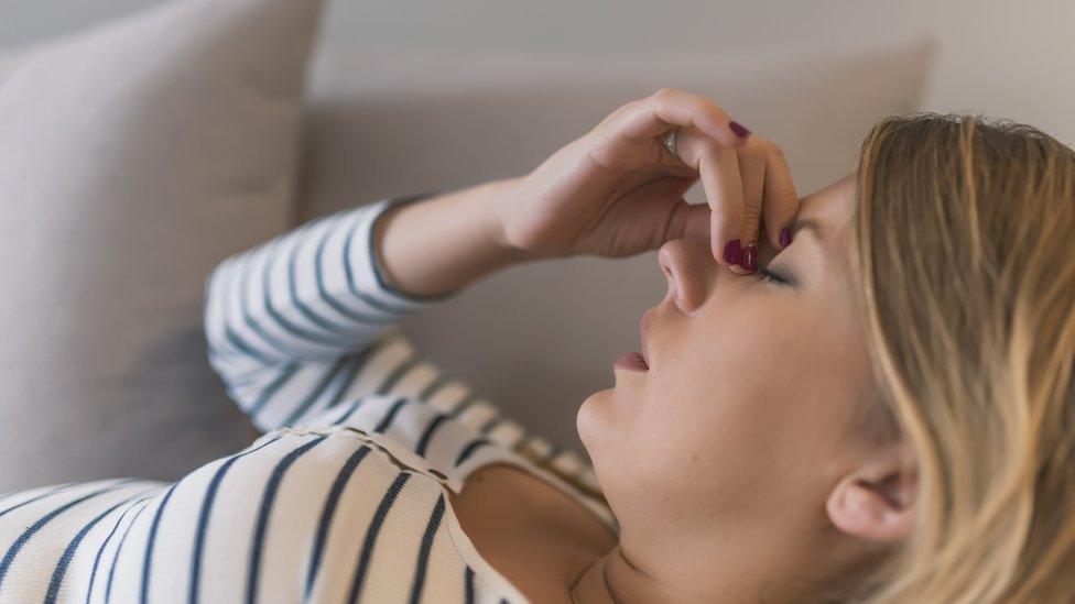 A woman suffering fatigue holds her head in her hand