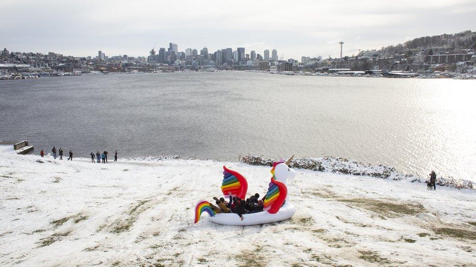 A group of people fly down a hill, overlooking city skyline, on a unicorn float