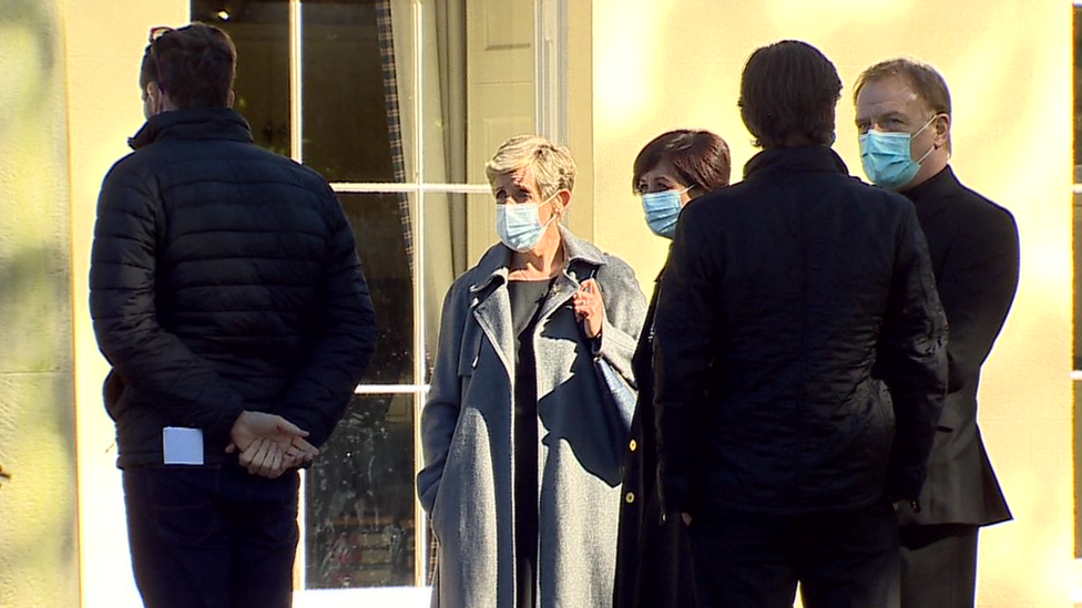 The actors and crew stand around wearing masks