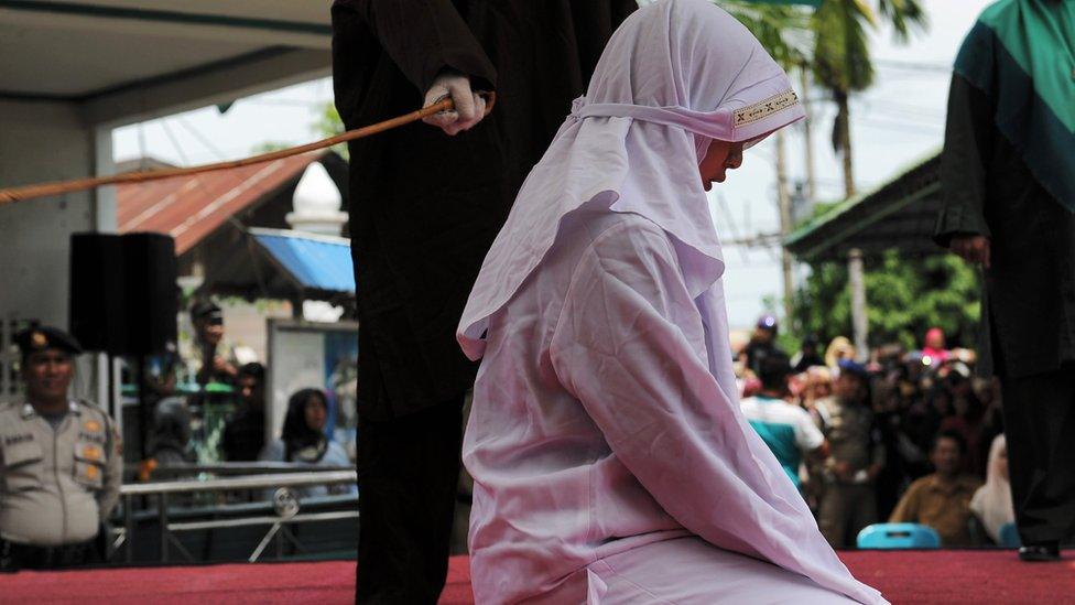 Indonesian woman kneeling on stage, about to be flogged