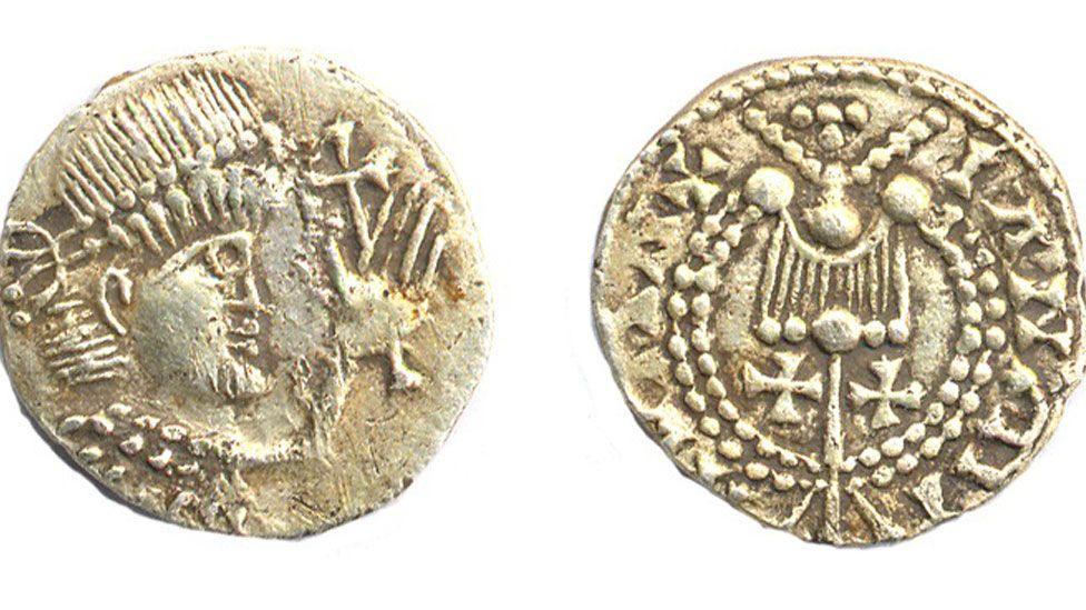 Two sides of a later Saxon gold coin. On the left is a close up of a man in profile, wearing a Roman-style diadem or headdress. His left hand is raised and behind it is a cross. On the right the coin has a lyre-shape above two crosses in the middle and a pattern of dots and symbols on the outside.