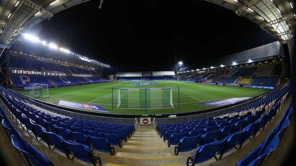 A wide view shot of the interior of the Weston Homes Stadium in Peterborough. It shows the blue seats behind one of the goals beyond which you can see the length of the pitch.