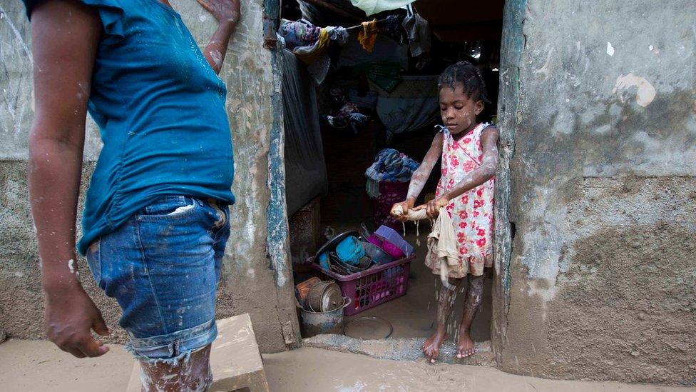 A girl helps her mother remove mud from her house after Hurricane Matthew flooded their home in Les Cayes, Haiti