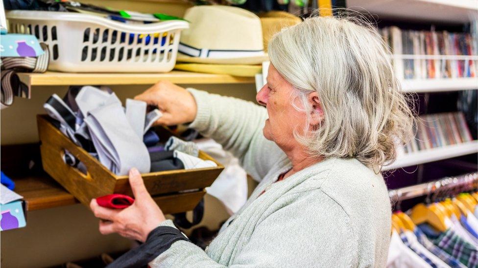 Older woman sorting ties in charity shop