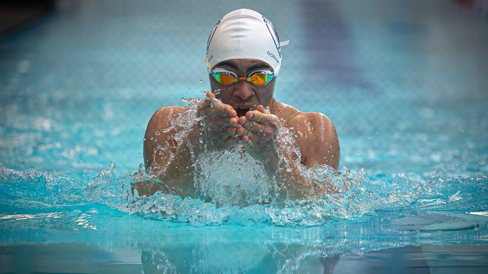 A man swimming in a pool heading towards the camera, wearing a white swim cap