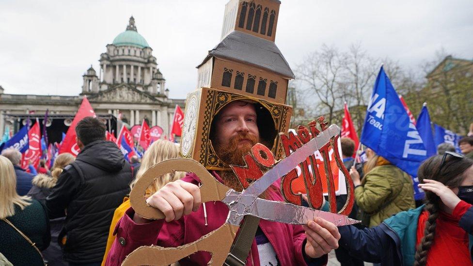 A teacher holding a pair of scissors saying 'No More Cuts'