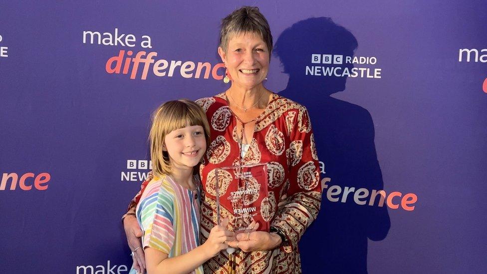 A young girl and a woman hold a glass award