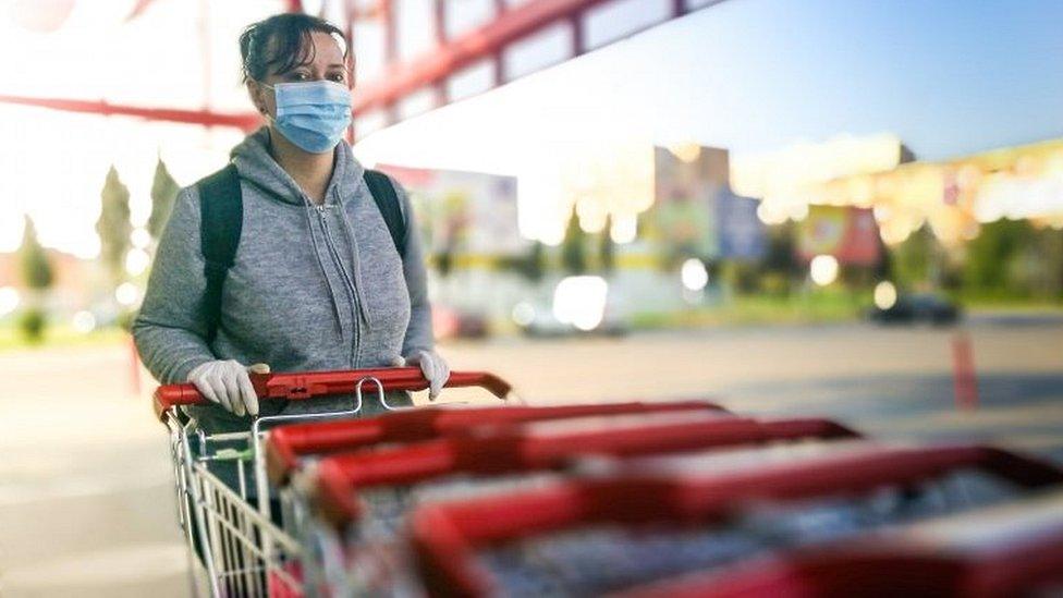 Woman in mask and gloves pushing shopping trolley