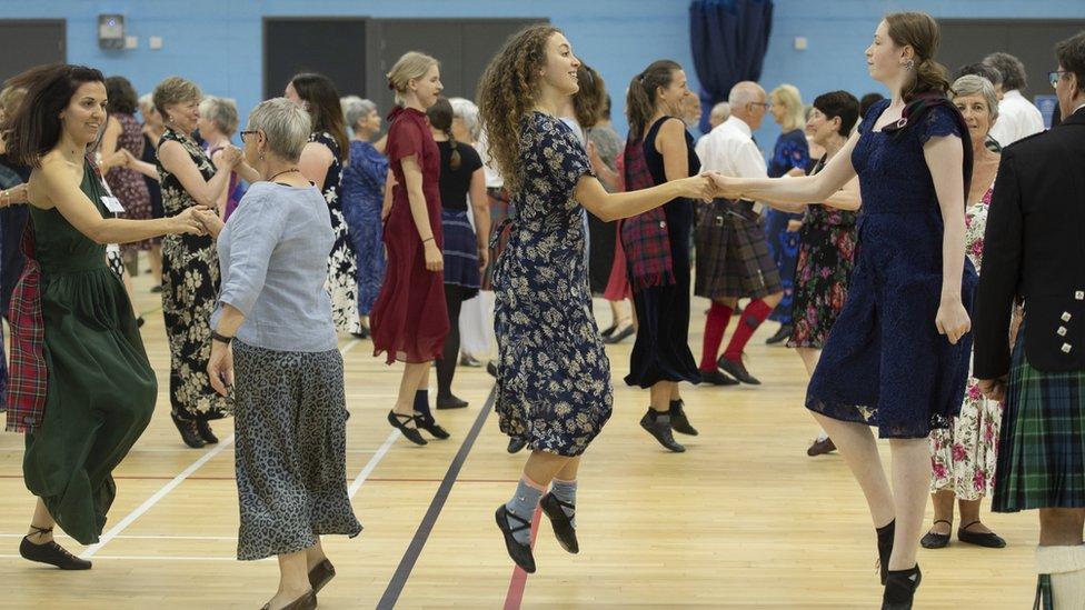 Group of Scottish country dancers with two female couplings in the foreground