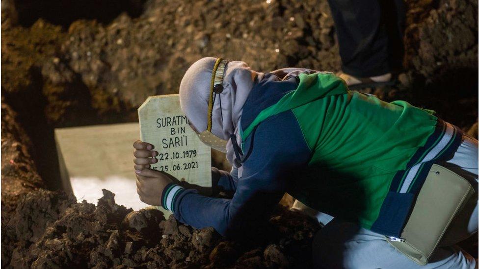 A family member wearing a face mask mourns during the burial of a relative