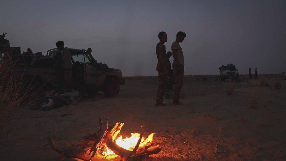 Vehicles and people near a camp fire in the desert