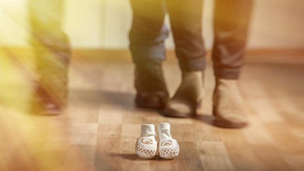 baby shoes next to adult feet