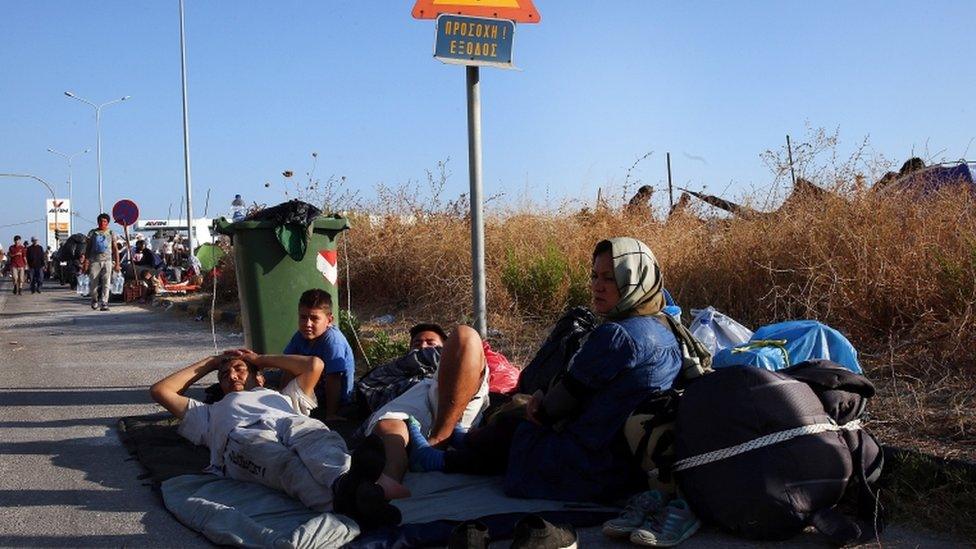 Migrants sit on a roadside near the site of the camp