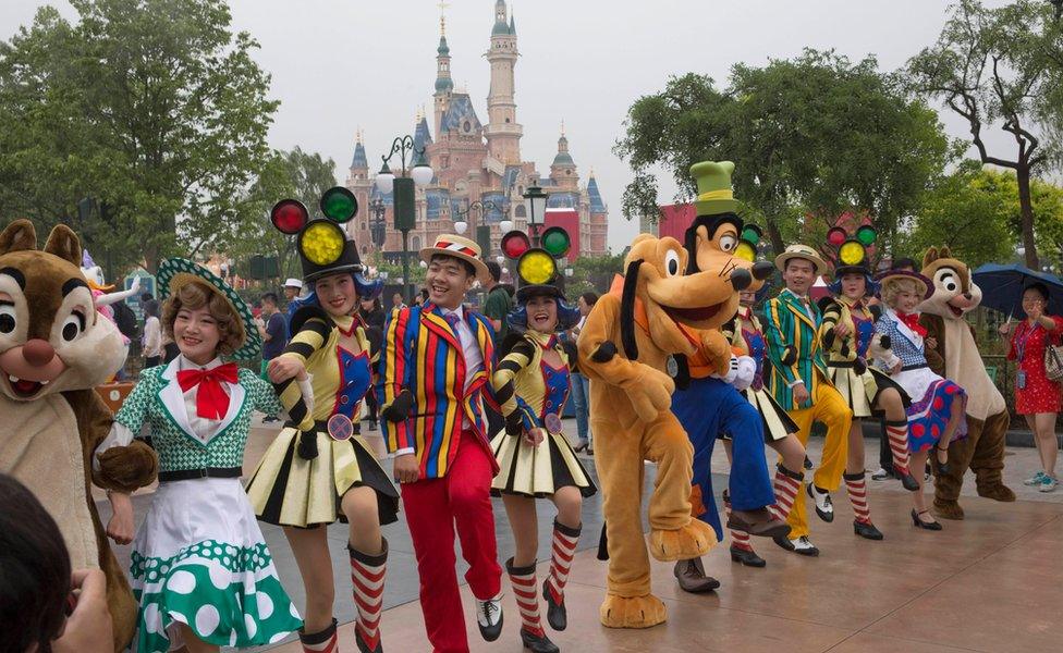 A line of Disney staff dressed in character and other costumes, dance during a parade at the park, with the centrepiece castle in the background, 15 June 2016.