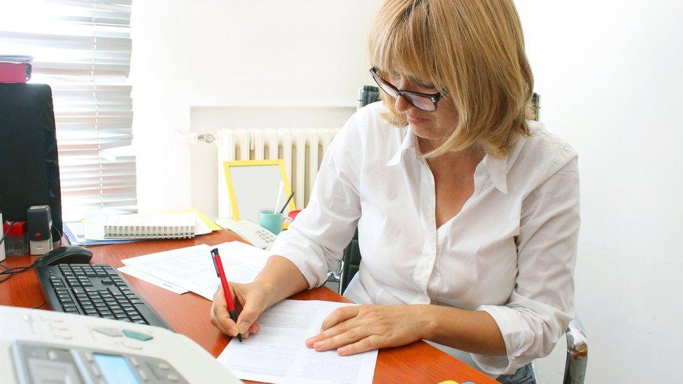 Woman sits writing at desk