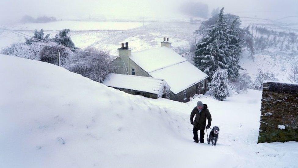 A dog walker negotiates heavy overnight snow in Carrshield in the Pennines, near Hexham in Northumberland