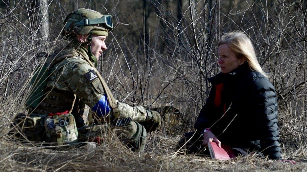 Arthur sits on the bare, scrub-laden ground with Orla Guerin, talking