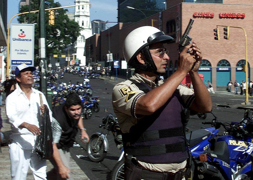 A policeman holds up his gun during clashes in Caracas April 11, 2002. At least ten people were killed and more than 80 injured as shooting broke out