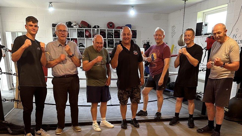 A group of men standing in a line, holding their hands up with boxing-style fists