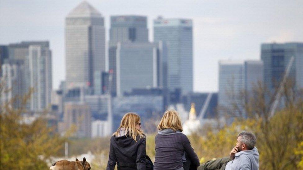 People sitting in Greenwich park with Canary Wharf in the background