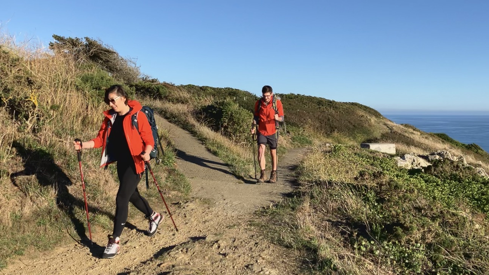 Woman and man walking along cliff path in hiking gear