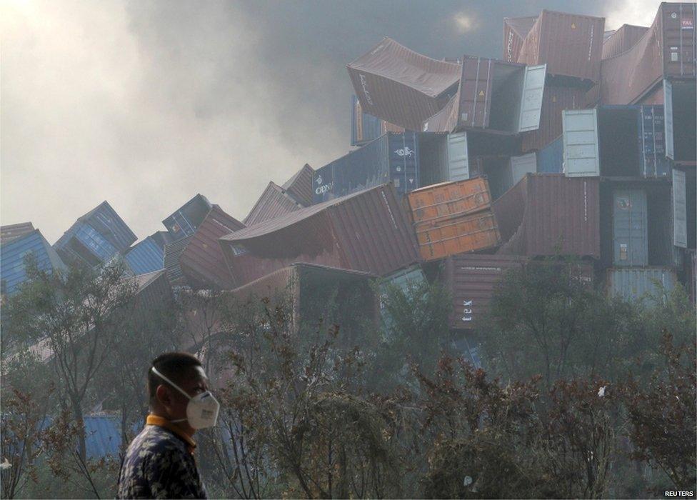 A man wearing a mask walks past overturned shipping containers after explosions hit the Binhai new district in Tianjin 13 August 2015