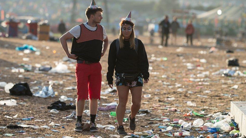 Two festival-goers standing in a field full of rubbish.