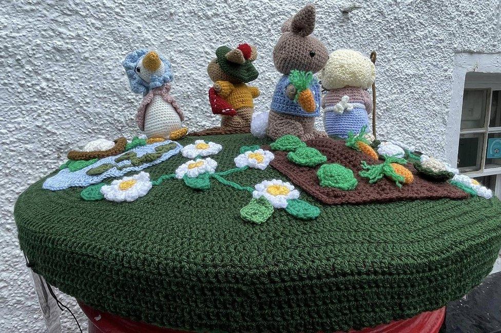 Four crocheted characters on a green mat on top of a post-box