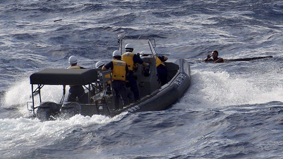 A handout picture made available by the Japan Coast Guard shows Japan Coast Guard rescue workers reaching out to the crew of a Chinese fishing boat that sunk following a collision with a Greek cargo vessel