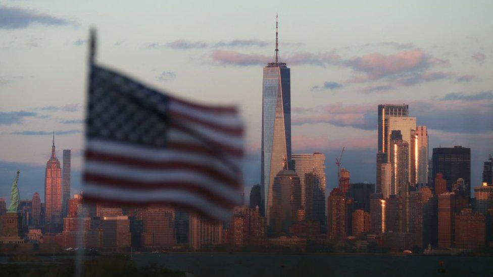 An American flag flies in front of The Statue of Liberty, the Empire State Building and One World Trade Center as the sun sets in New York City on December 15, 2019 as seen from Bayonne, New Jersey