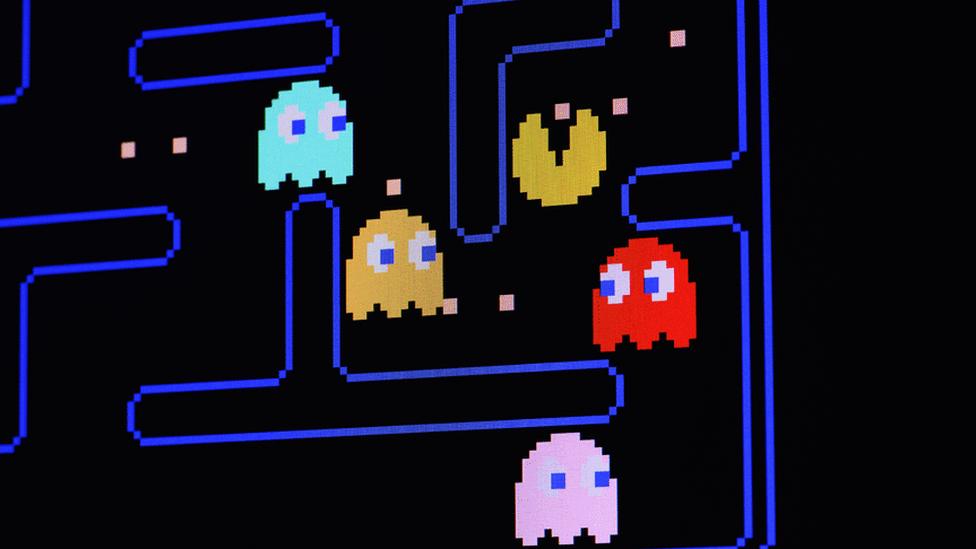 Pac-Man ghosts on the video game. Pac-Man is a yellow circle missing a triangle which acts as a mouth. The animation follows small pink dots around a black and blue maze and is pursued by four animated ghosts - one blue, one red, one yellow and one pink.