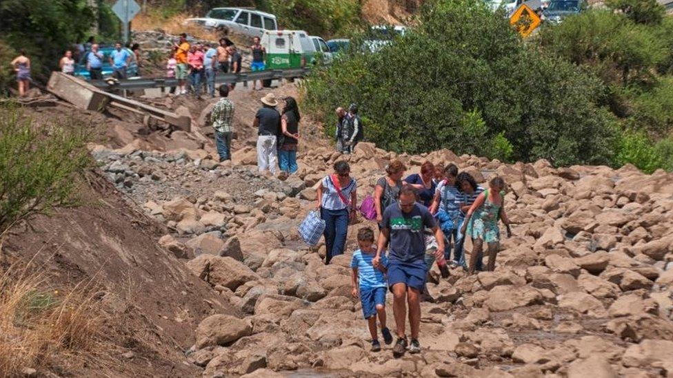 People walk along a damage road after a flood near Santiago, Chile February 26, 2017.