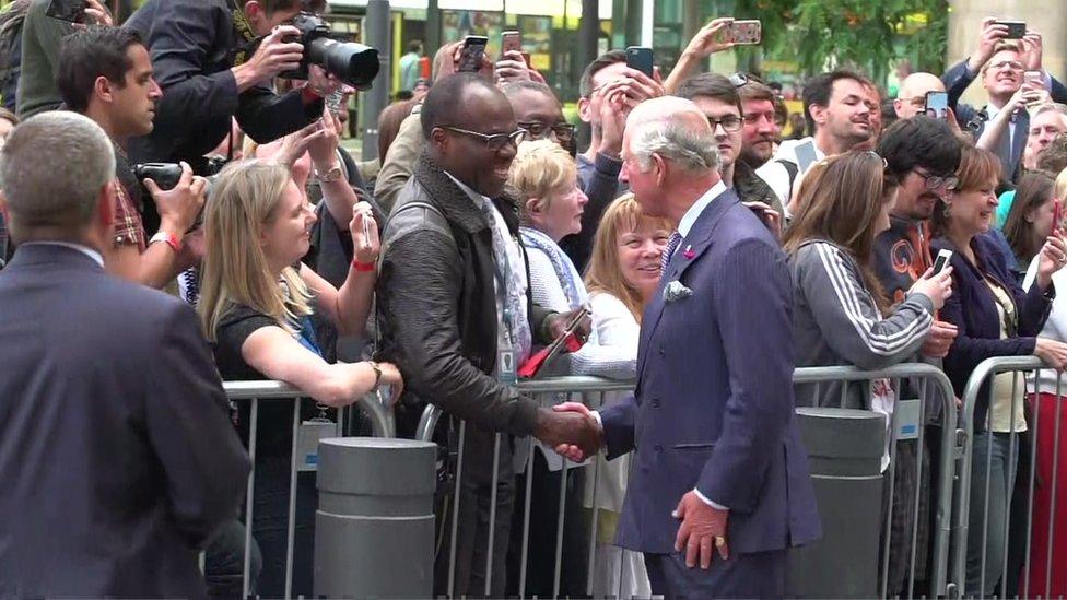 Prince Charles shaking hands with a man in front of a crowd in Manchester