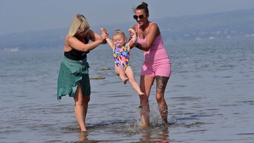 Women swinging child in ocean