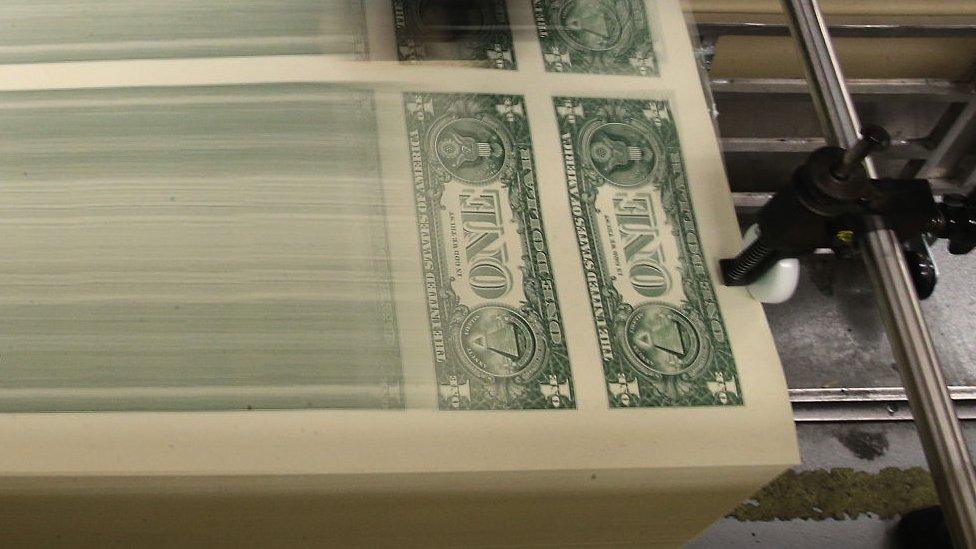 Dollar bills roll off a US government printing press.