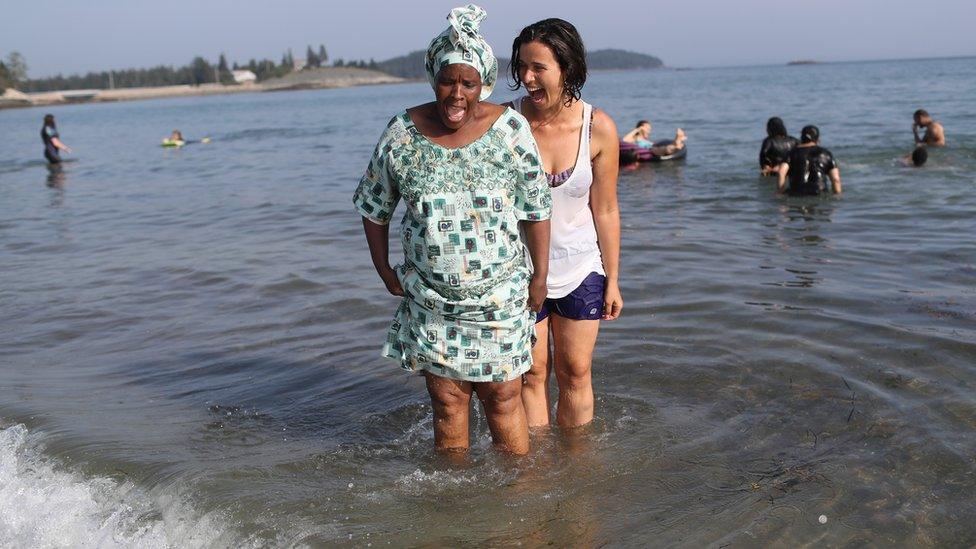 A Congolese woman stands in the ocean for the first time guided by an American woman during during a programme to help integrate new refugees in Maine, the US - Tuesday 28 August 2018