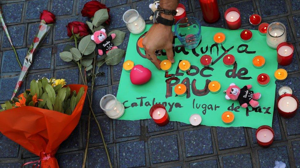 A person places a candle on a placard, reading in Spanish and Catalan "Catalonia, place of peace", in the area where a van crashed into pedestrians at Las Ramblas street in Barcelona