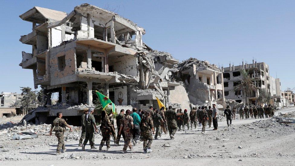 Troops from the Syrian Democratic Force (SDF) marching past a ruined building in Raqqa, Syria