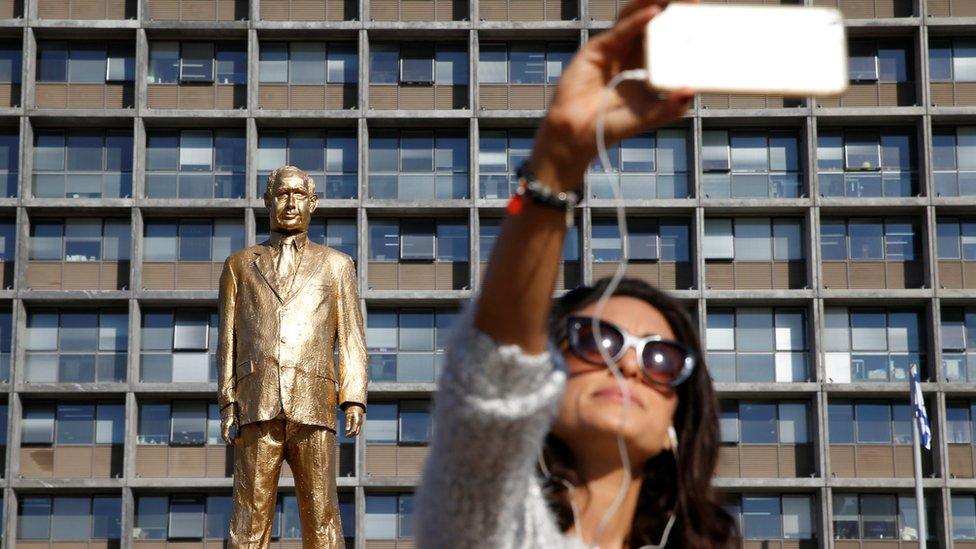 A woman takes a selfie in front of the golden Netanyahu statue