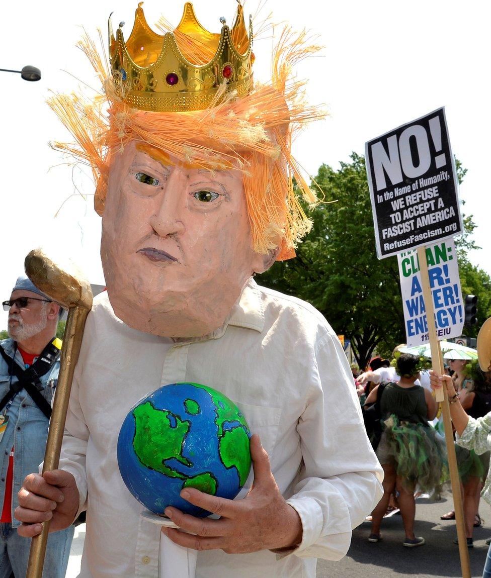 A protester in a costume depicting Trump holds an Earth and a golf club as he joins demonstrators moving down Pennsylvania Avenue during a People's Climate March,