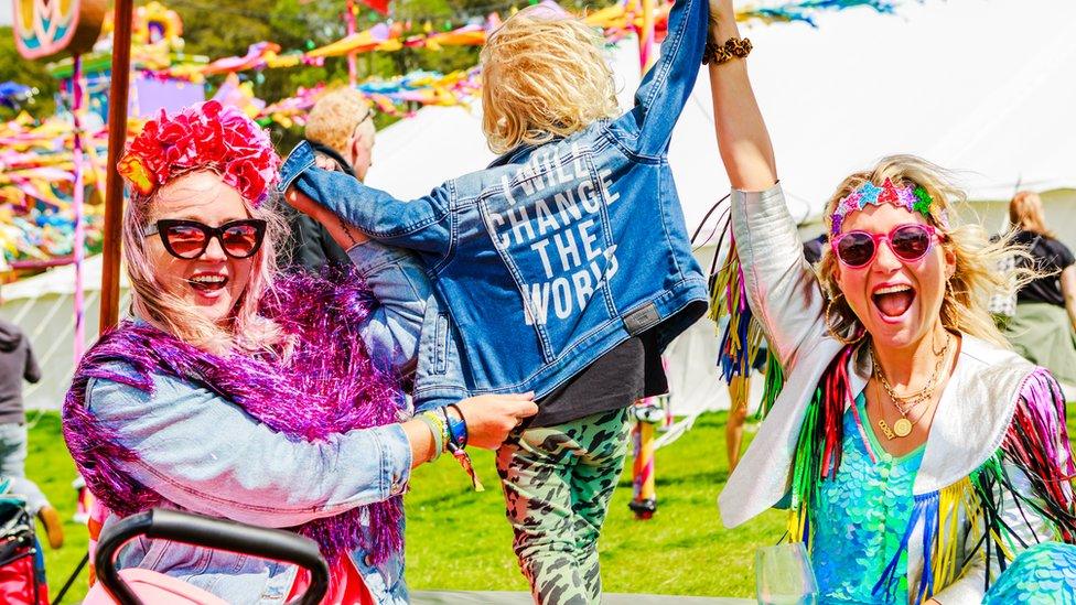 Two women in bright outfits with a child whose jacket bears the message 'I will change the world'