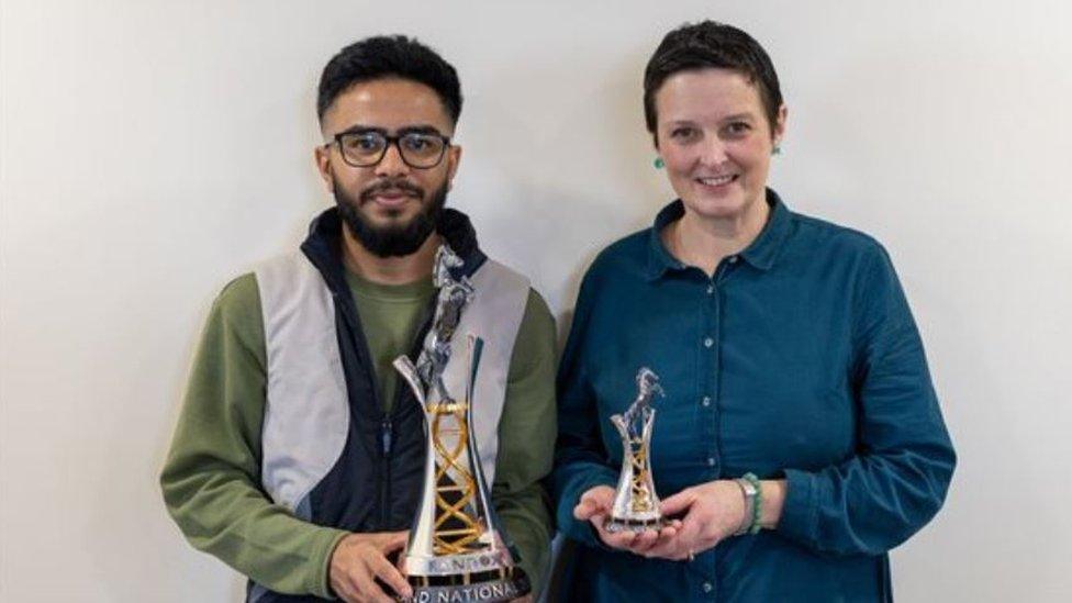 Student Ritik Tailor (left) holds the 2024 Randox Grand National trophy with silversmith Cara Murphy