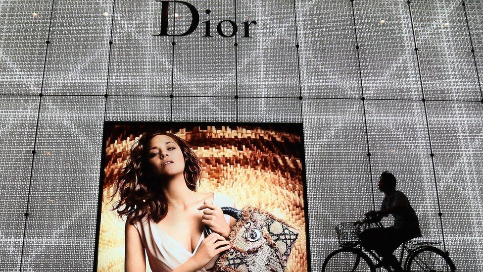 A Chinese man rides bicycle past an advertisement for the Christian Dior store on June 8, 2012 in Beijing, China