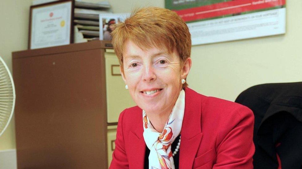 Former Post Office chief Paula Vennells is seen sitting sitting behind a desk while looking into the camera and smiling