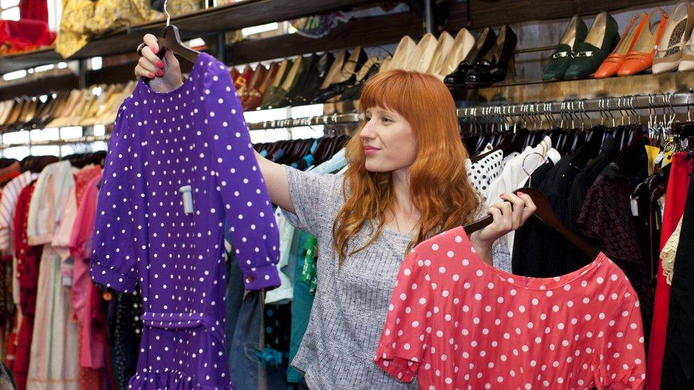 Woman holds up two dresses whilst shopping