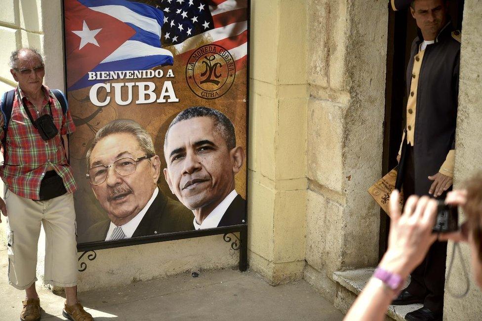 A tourist poses for a picture with a sign placed at the entrance of a restaurant with the images of Cuban and US Presidents Raul Castro and Barack Obama in Havana, Cuba