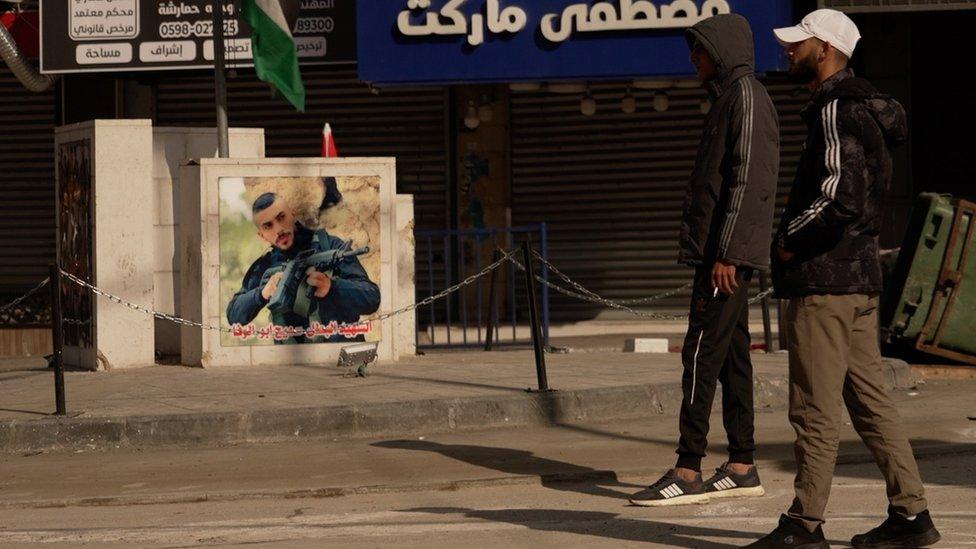 Two youths walk near a picture of a young man with an assault rifle. Photo: 12 December 2023