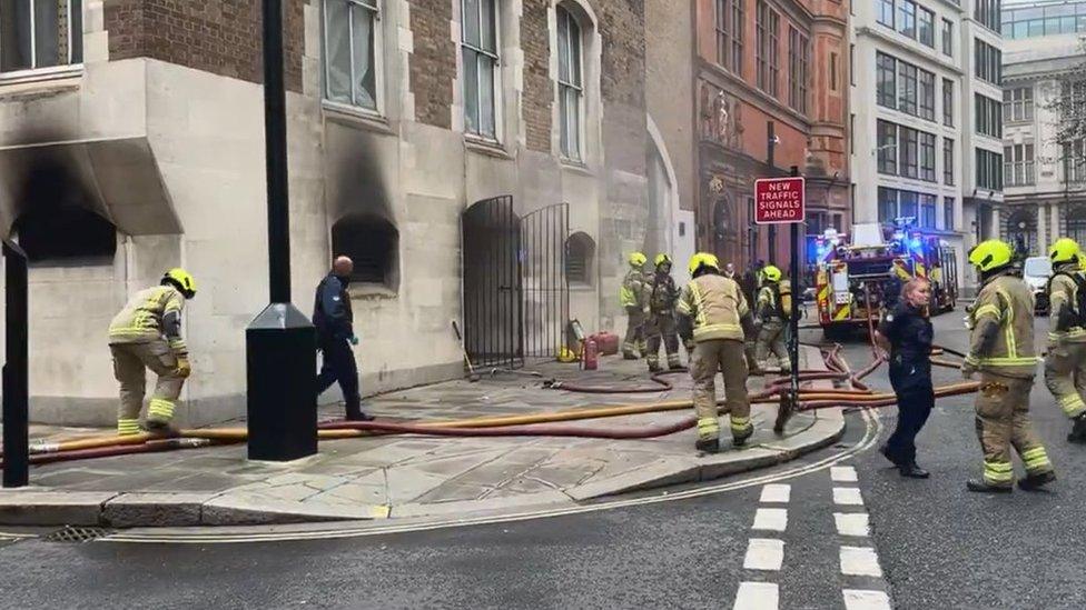 Firefighters crowd around a building next to the Old Bailey where black smoke marks are seen on a wall