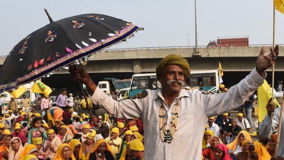 A farmer stands with an umbrella in Delhi during the protest