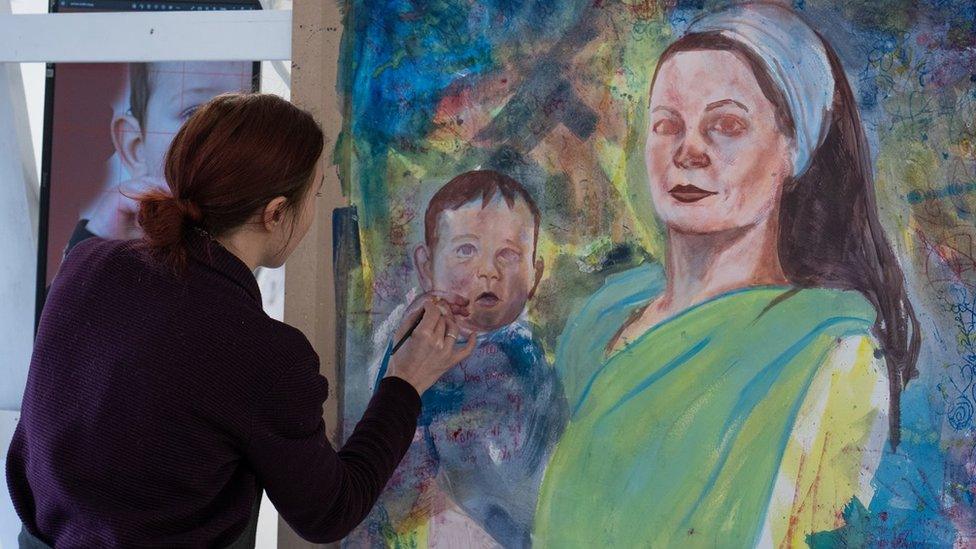 A woman paints a large picture of a woman holding a baby